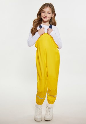 Geltoni nepralaidūs darbo drabužiai su reguliuojamomis tamsiai mėlynomis petnešomis, su kelio pagalvėlėmis ir atspindinčiais akcentais. Užsidėti ant baltos ilgomis rankovėmis marškinėlių.