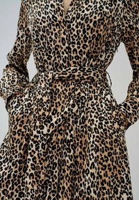 Abito leopardato in beige e nero, realizzato in tessuto morbido, con maniche lunghe, vita con cintura e tasche laterali.