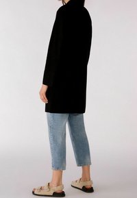 Svart långärmad cardigan med mjuk textur, ihop med ljusblå jeans med uppvikta ben. Bärs med beige tofflor i fuskpäls med spänne.