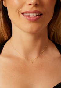 Collier de couleur or avec une chaîne délicate, orné d'un petit pendentif en forme de "F". La texture est lisse et le design minimaliste.
