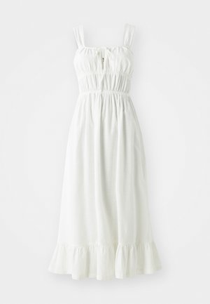 Robe en lin blanc avec un corsage froncé, des bretelles ajustables et un ourlet à volants. Elle présente un détail en trou de serrure à l'avant.