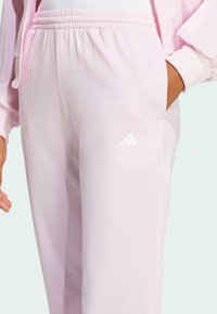 Lys rosa joggebukse laget av mykt stoff, med elastisk midje og en liten hvit Adidas-logo på venstre bein.