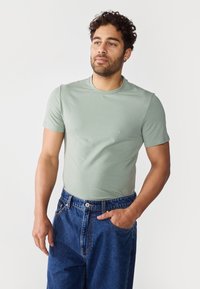 Mintgrønn t-skjorte med korte ermer laget av mykt stoff, kombinert med blå denimjeans, med en avslappet passform og klassisk rund hals-design.