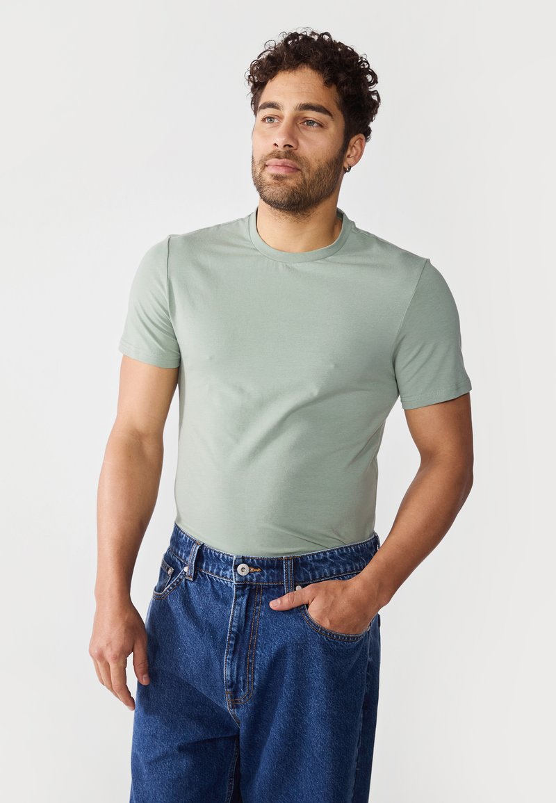 Mintgrønn t-skjorte med korte ermer laget av mykt stoff, kombinert med blå denimjeans, med en avslappet passform og klassisk rund hals-design.