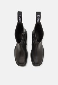 Black leather ankle boots with a square toe, side zipper, and a contrasting fabric pull tab featuring "Camper" logo in white.