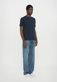 Marineblå kortermet t-skjorte kombinert med lyseblå vide jeans og hvite sneakers, med et enkelt design og en avslappet passform.