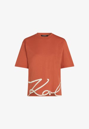 Rostfarget bomull t-skjorte med korte ermer og rund hals, med hvit "Karl" signaturgrafikk på forsiden. Glatt tekstur.