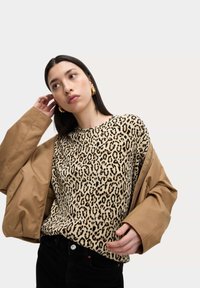Maglione con stampa leopardata in tessuto beige e nero, dalla vestibilità rilassata. Giacca color nocciola indossata sopra, con una texture liscia e maniche extra-large.