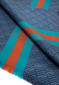 Écharpe à motif géométrique bleu marine, avec des rayures teal et rouille. Texture lisse avec bords à franges et designs linéaires complexes.