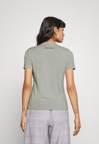 Camiseta de algodón de manga corta en color verde claro, con un cuello redondo y el logo "Calvin Klein" impreso en negro en la parte superior de la espalda.