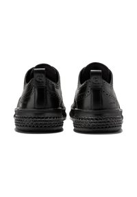 Černé kožené boty s perforovanými detaily, kulatou špičkou a texturovanou gumovou podešví. Obsahují malý patní pásek pro snadné obouvání.