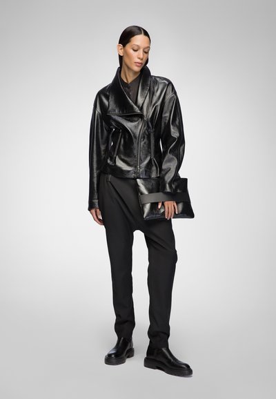 Black leather motorcycle jacket with a shawl collar, zippered front, paired with loose-fitting black trousers and a clutch bag. Black boots.