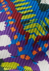 Tessuto colorato con una trama a coste texturizzata e vivaci disegni floreali in tonalità di viola, blu, verde, arancione e bianco.