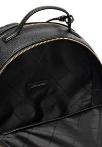 Wnętrze czarnego skórzanego plecaka z pikowanym wzorem. Zawiera złoty zamek błyskawiczny, czarną podszewkę z tkaniny oraz metkę z logo "Michael Kors".