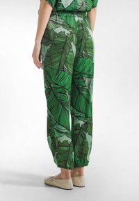 Zielone spodnie z liściastym wzorem, z elastyczną talią i ściągaczami przy kostkach. Wykonane z lekkiego materiału o gładkiej fakturze.
