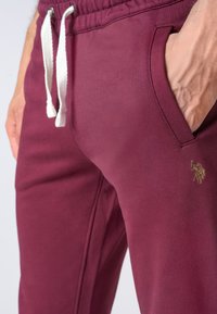 Pantaloni della tuta bordeaux realizzati in morbido cotone misto, con vita regolabile tramite cordino, tasche laterali e un piccolo logo dorato.