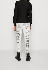 Maglia nera a maniche lunghe con texture abbinata a jeans bianchi a lavaggio acido. I jeans hanno una vestibilità ampia e sono indossati con stivaletti neri alla caviglia.