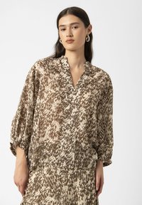 Bluse aus Bronze und Creme mit Muster, V-Ausschnitt und Ballonärmeln, aus einem leichten Stoff, mit strukturierter Oberfläche.
