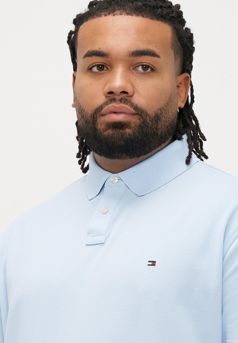 Light blue polo shirt made of textured fabric, featuring a three-button placket and a small logo near the chest.