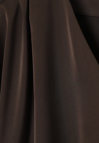 Tissu lisse de couleur marron foncé avec des plis doux et des détails de couture subtils dans le coin supérieur droit.