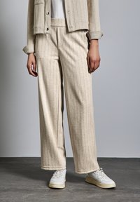 Ljusbeige vide byxor i mjukt tyg med vertikala ränder, i kombination med vita sneakers. Byxorna har framfickor och en avslappnad passform.
