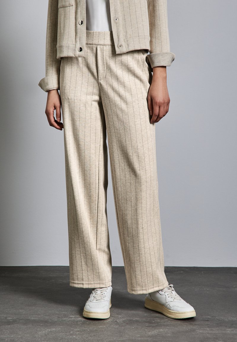 Ljusbeige vide byxor i mjukt tyg med vertikala ränder, i kombination med vita sneakers. Byxorna har framfickor och en avslappnad passform.