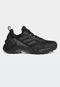 Chaussure de sport noire avec une tige en mesh, des accents texturés et une semelle épaisse en caoutchouc. Présente un renfort au bout et un système de lacets. Convient pour une utilisation en extérieur.