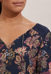 Marinblommig blus med V-ringning, kort ärm och färgglada blommönster i rosa, gult och vitt; slät textur.