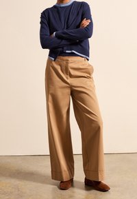 Maglietta a maniche lunghe blu navy con accenti azzurri, abbinata a pantaloni beige a gamba larga e stivaletti in suede marroni. Texture morbide e vestibilità sartoriale.