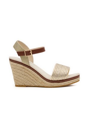 Sandalia con cuña tejida en beige con tiras marrones en el tobillo y hebilla, puntera abierta y suela de cuerda texturizada, mostrada de perfil sobre fondo blanco.