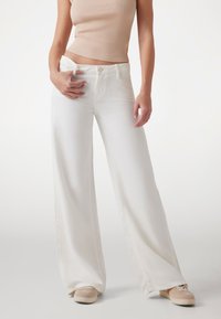 White wide-leg denim pants with a high waist, featuring a front button and zipper closure, paired with beige sneakers.