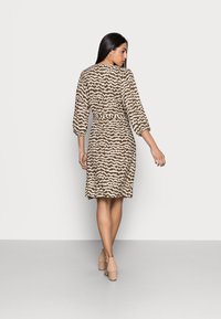 Vestido castanho com padrão, mangas de três quartos, uma cintura cingida com cinto e uma bainha até ao joelho. O tecido tem uma aparência texturada.