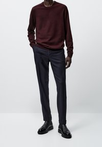 Viininpunainen neulepusero ja tummansiniset räätälöidyt housut. Mustat nahkaiset Chelsea-saappaat ovat sileäpintaiset ja niissä on paksu pohja.