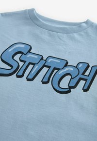 Šviesiai mėlyna medvilninė marškinėliai su ryškiai blizgiu mėlynu "STiTCH" užrašu. Minkšta tekstūra ir apvalus išpjovimas su trumpomis rankovėmis.