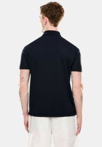 Polo de color marino con mangas cortas, que presenta un cuello y una textura suave. La vista trasera no muestra patrones ni acentos adicionales.