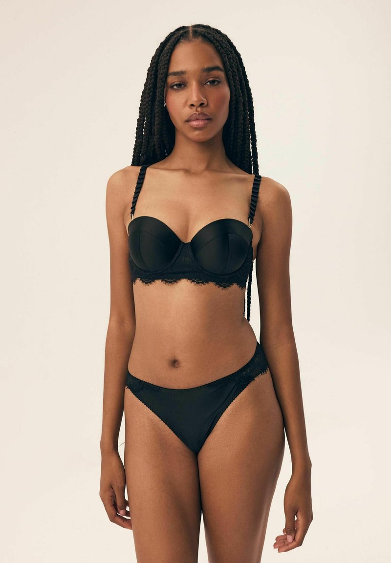 Czarny zestaw bielizny składający się z usztywnianego biustonosza z koronkowym wykończeniem i falbaniastymi ramiączkami, w połączeniu z pasującymi majtkami z koronkowymi akcentami.