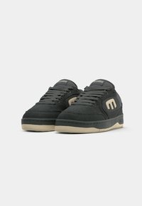 Black suede sneakers with a beige rubber outsole, featuring a rounded toe, lace-up closure, and a logo detail on the side.