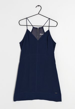 Marineblå ærmeløs kjole med tynde stropper, V-hals, lynlås bagpå og tætsiddende syninger, hængende på en sort tråd bøjle.