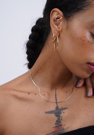 Gold necklace with a wavy design, paired with gold hoop earrings. Smooth texture, minimalistic style, and fine detailing enhance appearance.