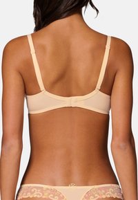 Beige bra with adjustable straps, a hook closure, and a smooth texture. Features floral accents on the back and a minimalist design.