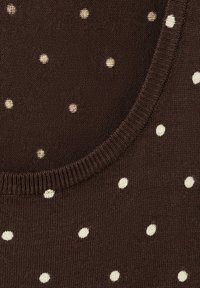 Gros plan sur un tissu en maille marron foncé à pois blancs avec un col arrondi bordé d'une bordure côtelée.