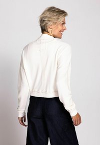 Gekürzter crèmefarbener Pullover mit langen Ärmeln, der eine strukturierte Rückennaht und gerippte Bündchen aufweist, kombiniert mit dunkelblauen weit geschnittenen Hosen.