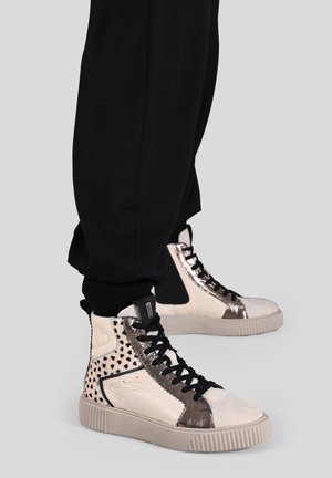 Des baskets montantes avec un mélange de matériaux, comprenant du beige lisse, de l'argent texturé et des accents à pois, avec un design à lacets noirs.