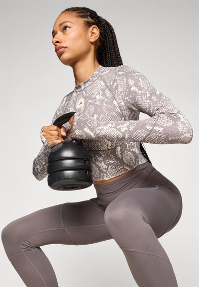 Langermet, slangeliknende, lysegrå topp med tettsittende ermer; mørkegrå leggings med sømmer; person som holder en svart kettlebell.