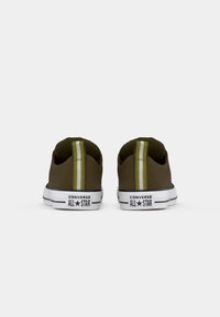 Un paio di sneakers Converse All Star verde oliva viste di spalle, con suole bianche e tiranti gialli a strisce sul tallone.