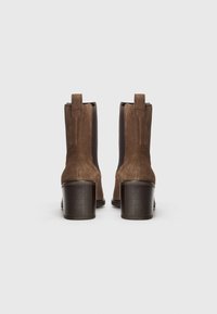 Bottines en daim marron avec des panneaux élastiques sur les côtés, une languette en boucle et un talon carré avec une finition texturée.