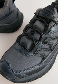 Mørkegrå og sorte atletiske sneakers med tekstureret stof, polstret krave og unik zigzag snøre design på tykk sål, vist tæt på.