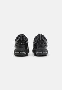 Chaussures de sport noires au design élégant, avec un mesh texturé, des accents réfléchissants et des semelles en caoutchouc, vues de l'arrière.