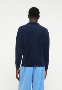 Navyblauer, kuscheliger Strickpulli mit Kragen, langen Ärmeln und einer leicht oversized Passform, kombiniert mit hellblauen, weiten Hosen.