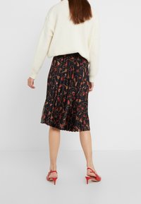 Svart plisserad kjol med ett blommönster i röd, beige och brun, tillsammans med en krämfärgad oversize-tröja och röda klacksandaler.